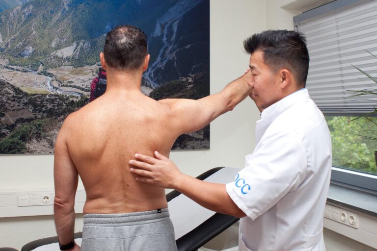 Orthopedisch specialist John Cheung onderzoekt arm- en rugmobiliteit van patiënt in kliniek in Amsterdam.